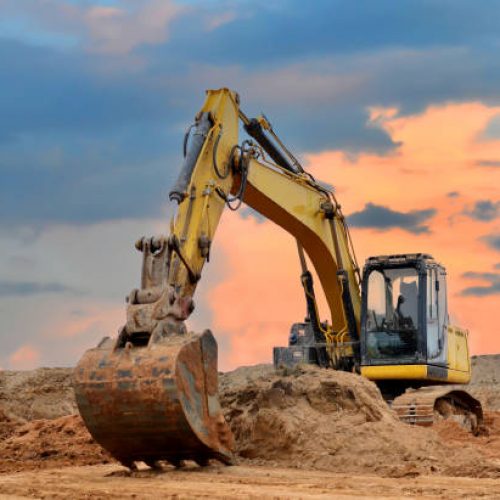 Excavator working on earthmoving at open pit mining on sunset background. Backhoe digs sand and gravel in quarry. Heavy construction equipment during excavation at construction site